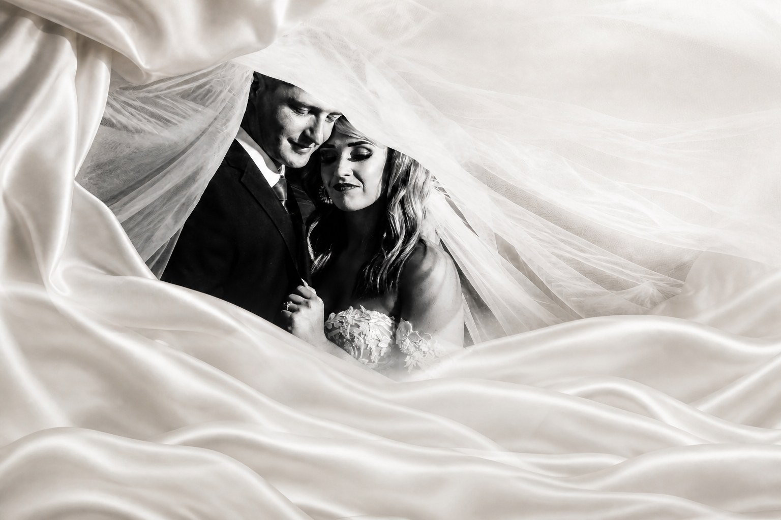 Bride and groom framed by a flowing veil and ivory satin
